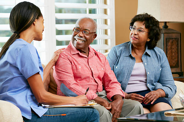 Nurse Making Notes During Home Visit With Senior Couple Smiling